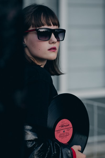 Wearing dark sunglasses and jackets woman holding a vinyl record
